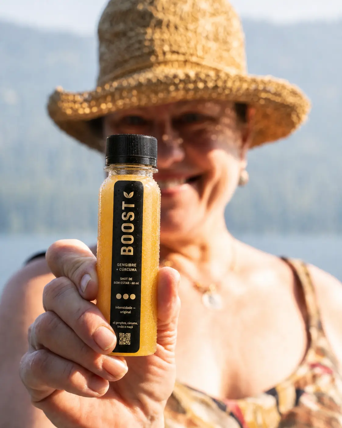 Mulher segurando um shot Boost Original de 60 ml em frente a um lago